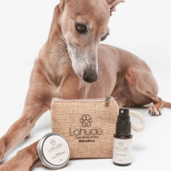 Galgo junto al neceser de Lahude, bálsamo hidratante regenerador y spray reparador en tamaño mini.
