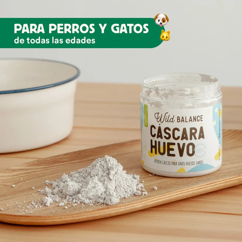 Bote abierto de Wild Balance Cáscara de Huevo con su contenido en polvo sobre tabla de madera, suplemento para perros y gatos.