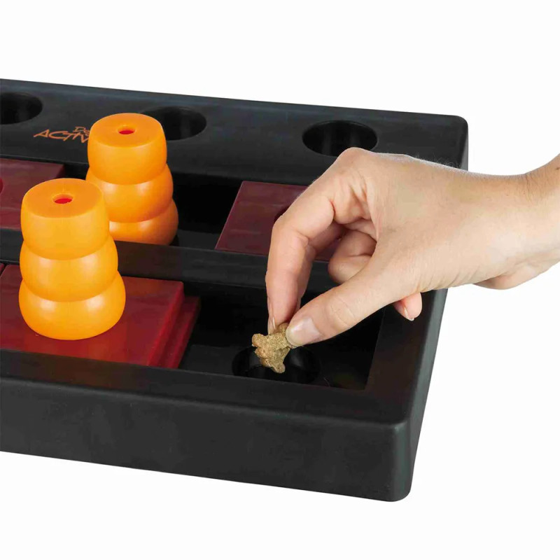 Detalle del juego Dog Activity Chess Nivel 3 con una mano colocando un snack en el compartimento, preparación del juego de intel
