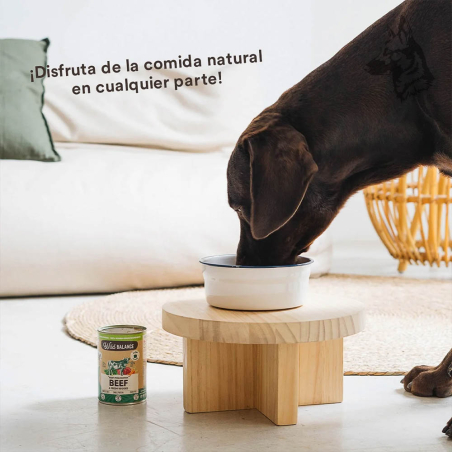 Un perro disfruta de su comida en un comedero elevado, con la lata de Wild Balance Beef & Fresh Veggies al lado, destacando su p