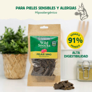 Un paquete de Wild Snacks Pelaje Sano de Venado sobre una mesa blanca, con el texto “Para pieles sensibles y alergias – Hipoalergénico” en la parte superior. A su lado, un pequeño montón de snacks y un frasco con ingredientes naturales, destacando su alta digestibilidad.