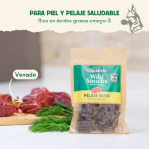 Un paquete de Wild Snacks Pelaje Sano de Venado en una cocina, junto a un corte de carne de venado fresco y ramas de eneldo. El texto en la imagen resalta que el snack es rico en ácidos grasos omega-3 para una piel y pelaje saludable.